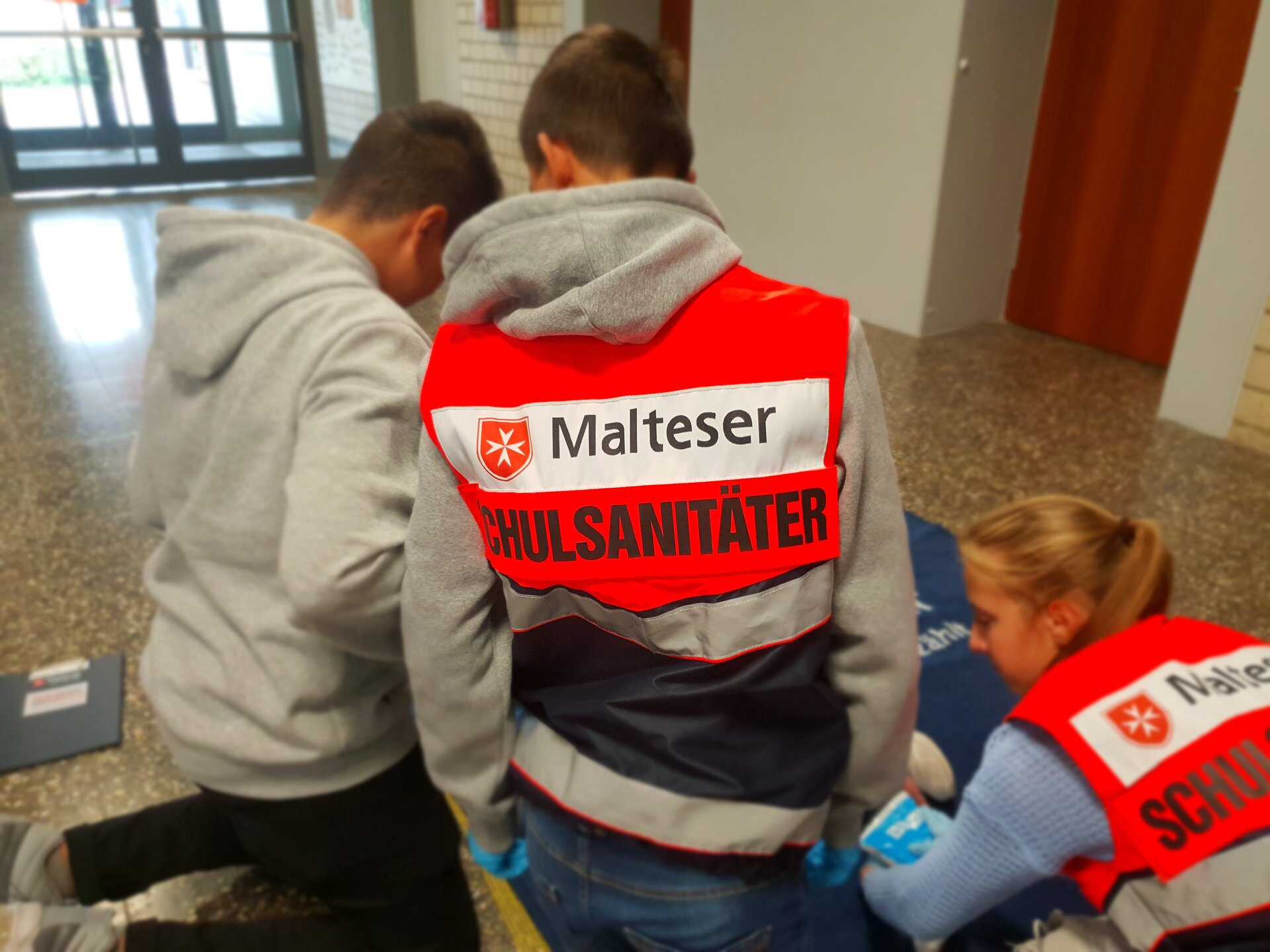 Foto von drei Malteser Schulsanitätern, die sich über etwas beugen.